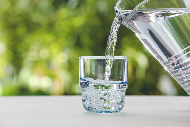 Verter agua dulce del frasco en un vaso sobre la mesa al aire libre, de cerca - Foto, Imagen