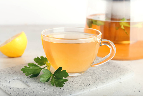 Tetera y taza de té caliente, perejil y limón sobre fondo claro - Foto, imagen