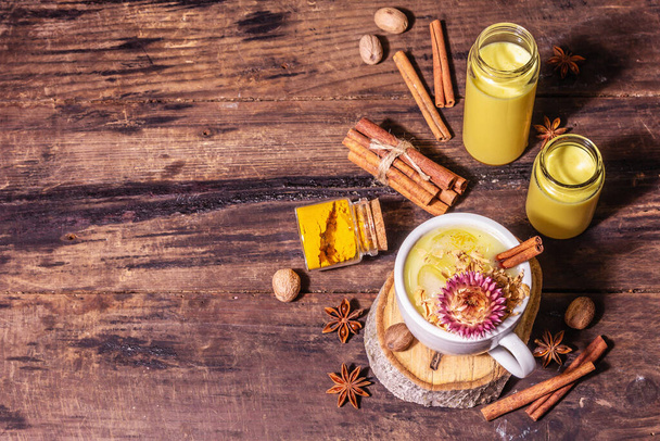 Golden turmeric milk with ice. Cinnamon, nutmeg, anise spices. Healthy morning breakfast drink concept. A modern hard light, dark shadow, old wooden table, top view - Fotografie, Obrázek