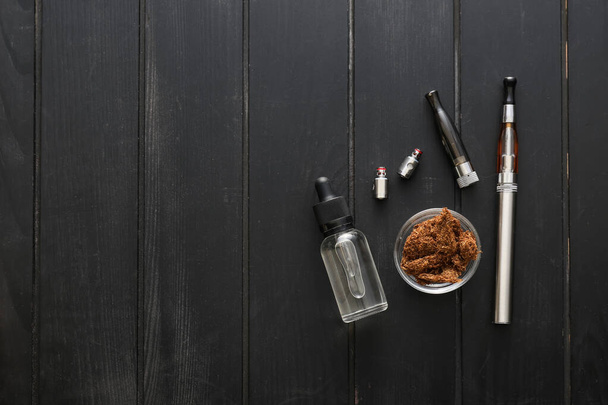 Electronic cigarette with oil and tobacco on dark wooden background - Zdjęcie, obraz
