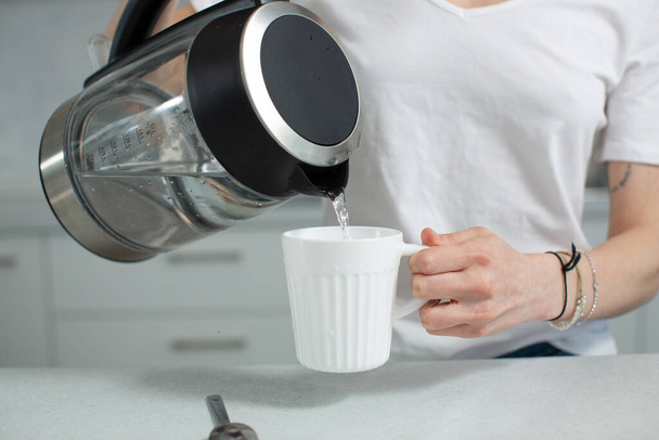A girl in a white T-shirt pours clean water from the kettle into a white mug - Photo, image