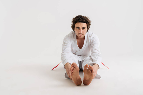 Selbstbewusster junger Karate-Mann wärmt sich isoliert vor weißem Hintergrund auf - Foto, Bild