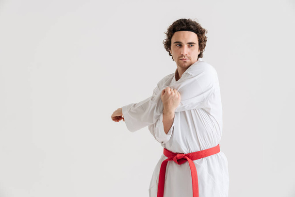 Young caucasian sportsman dressed in kimono practice in karate isolated over white background - Foto, imagen