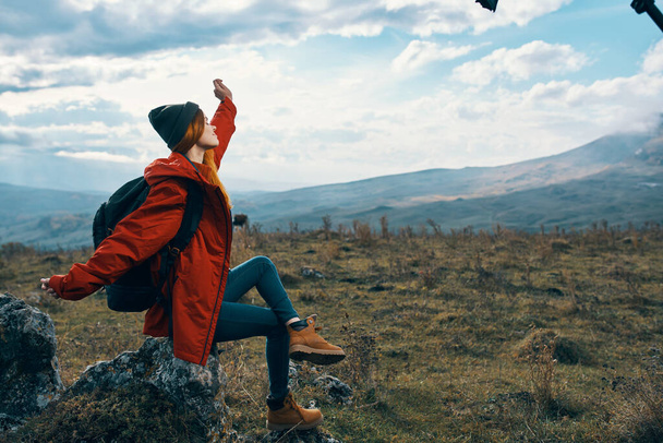 mujer viajero en una chaqueta se sienta en la piedra grande y mira el paisaje de las montañas - Foto, Imagen