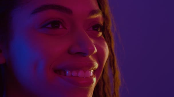 Retrato de perfil semi de una joven afroamericana positiva sonriendo, mirando a un lado el espacio libre con luces de neón - Metraje, vídeo
