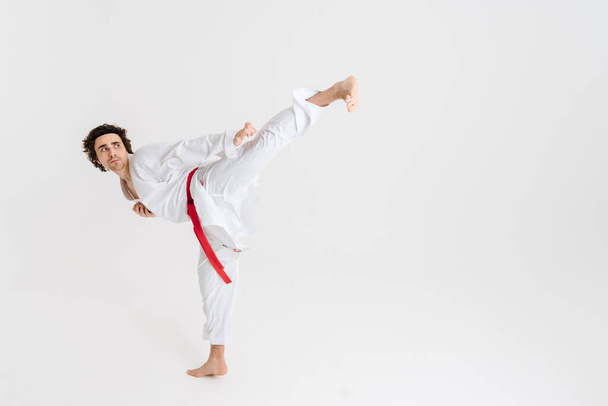 Young caucasian sportsman dressed in kimono practice in karate isolated over white background - Foto, Imagem