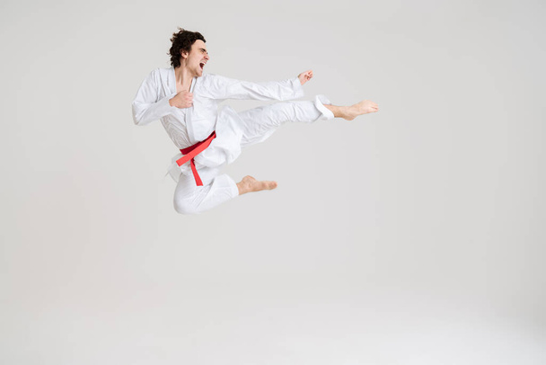 Young caucasian sportsman dressed in kimono practice in karate isolated over white background - Foto, Imagen