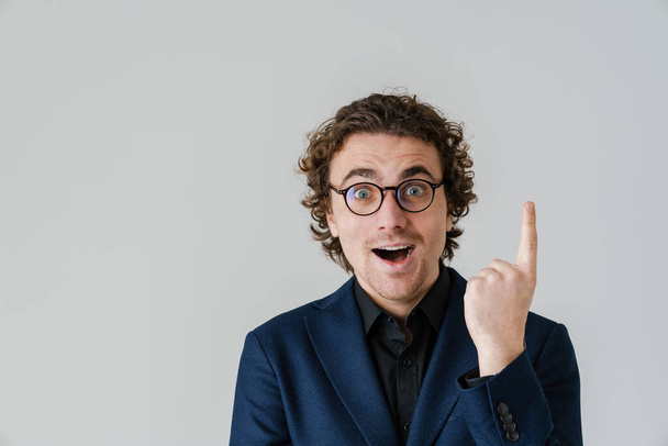 Surprised handsome man in eyeglasses exclaiming and pointing finger upward isolated over white background - Foto, imagen