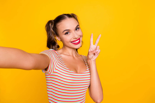 Photo of lady take selfie showing v-sign toothy smile wear striped shirt isolated yellow color background - Fotografie, Obrázek