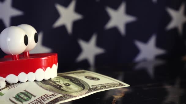 Una protesi giocattolo tiene una banconota da un dollaro tra i denti sullo sfondo della bandiera americana . - Filmati, video