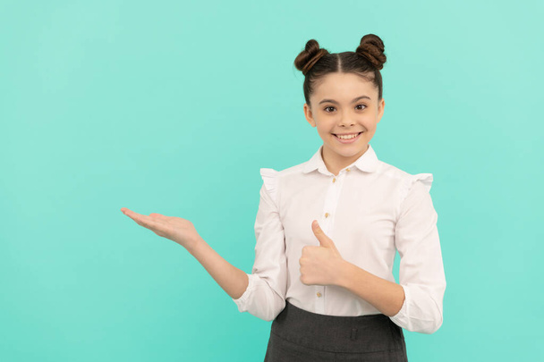 Щаслива дівчинка початкової школи дитина дає великі пальці, показуючи жест відкритої руки, представляючи продукт назад до школи продаж синього фонового простору копіювання, покупки
. - Фото, зображення