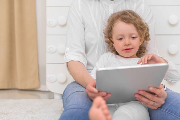 Uma menina com sua mãe olha para o computador tablet. - Foto, Imagem