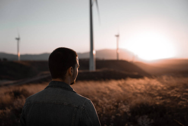 De mens denkt tijdens het kijken naar de zonsondergang omringd door windmolens - Foto, afbeelding