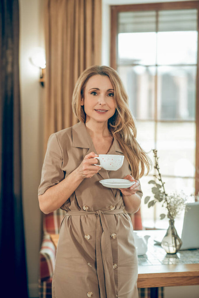 Long-haired elegant woman having tea and looking contented - 写真・画像
