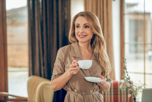 Long-haired elegant woman having tea and looking contented - Fotó, kép
