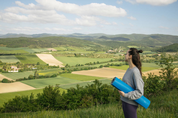 Woman with rolled fitness mat in her hands in the mountains - Photo, Image
