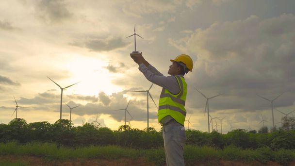 Portrait d'un ingénieur de moulin à vent asiatique, travailleur travaillant, tenant un modèle sur place dans un champ ou une ferme d'éoliennes, source d'énergie propre. Technologie écologique pour l'électricité. industrie nature environnement. Les gens - Photo, image