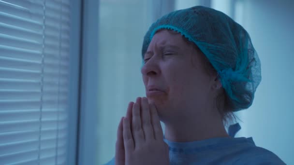 Mujer estresada con lesiones faciales llorando y rezando en el hospital antes de la cirugía. El paciente preocupado en la clínica con las manos cerradas pide ayuda a Dios. Persona tras accidente asustada y reza en ambulancia - Imágenes, Vídeo