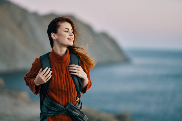 belle femme dans un pull tient un sac à dos sur le dos et parle en arrière-plan océan air frais - Photo, image