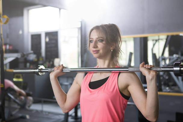 Cheerful young sportswoman doing barbell push press exercise at the gym - Foto, afbeelding