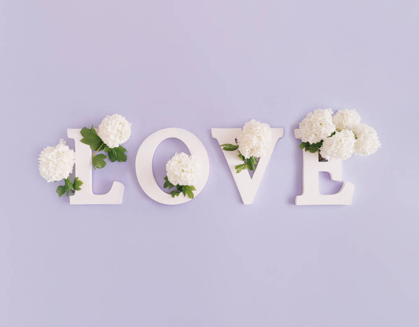 Λέξη αγάπης φτιαγμένη από λευκά γράμματα και όμορφα λευκά λουλούδια. Μήνυμα άνοιξης. Ελάχιστη έννοια της φύσης. Επίπεδη σκηνή. - Φωτογραφία, εικόνα