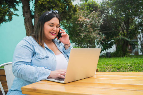 Plus size woman talking on the phone and using laptop. - Foto, imagen