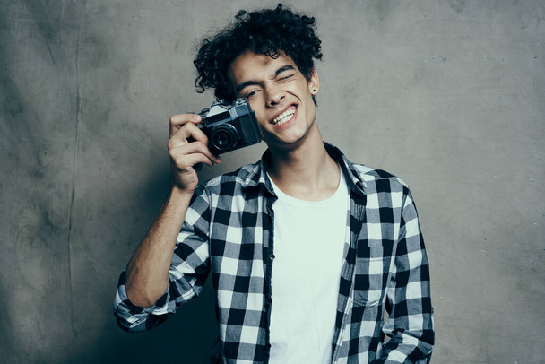 φωτογράφος σε καρό πουκάμισο με φωτογραφική μηχανή στο χέρι του σε γκρι φόντο σε δωμάτιο στούντιο χόμπι - Φωτογραφία, εικόνα