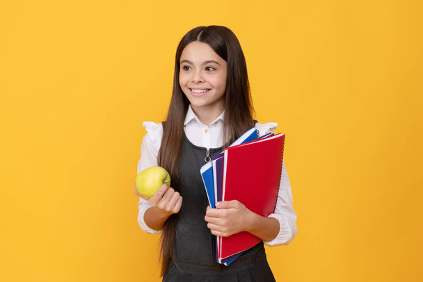 Niña feliz volver a la escuela sosteniendo manzana y libros fondo amarillo, día del conocimiento - Foto, Imagen
