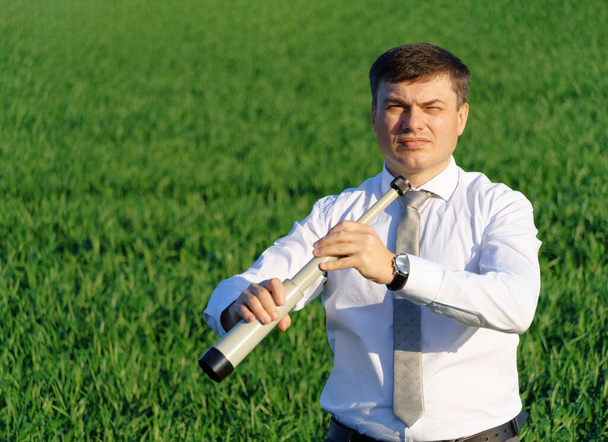 Бизнесмен позирует со шпилькой, смотрит вдаль и что-то ищет, зеленая трава и голубое небо на фоне - Фото, изображение