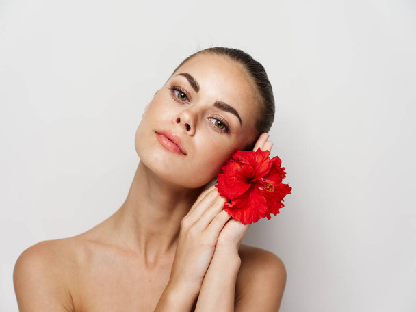 Güzel bir kadın elinde kırmızı bir çiçek tutuyor. Kırpılmış manzara kozmetik ürünleri izole edilmiş arka plan. - Fotoğraf, Görsel