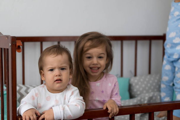 Sevimli, neşeli 3 çocuk kız ve erkek kardeş gri bebek beşikteki anaokulu çocukları pijamalarıyla uyanıp bacaklarını sallayarak uyanmışlar. Çocukluk, rahatlık, rahatlık, ilaç, sağlık konsepti - Fotoğraf, Görsel