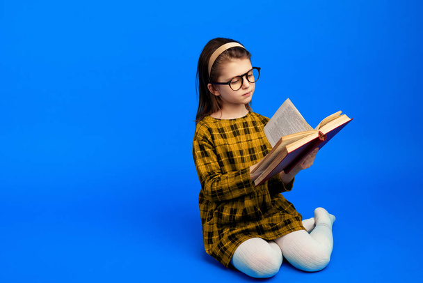 Šťastné dítě čtení knihy a posezení na modrém pozadí  - Fotografie, Obrázek