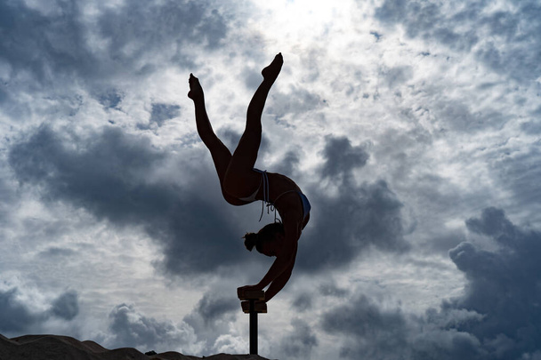 Flexible female circus Artist doing handstand against amazing cloudscape. Willpower, potential and desire concept - 写真・画像