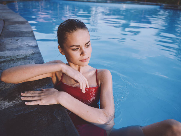a woman in a red swimsuit sits in the pool with her elbows on the tile with her hands - Valokuva, kuva