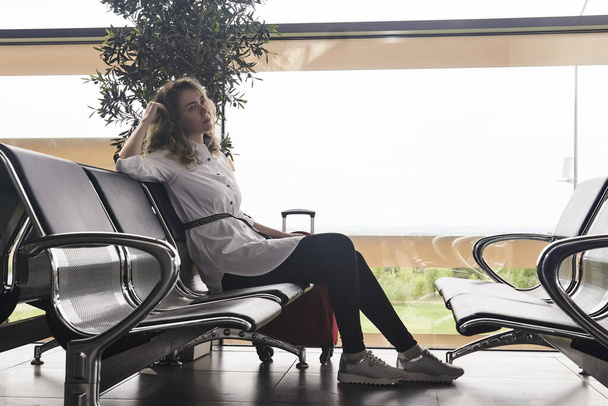 молода жінка турист з валізами сидить в залі очікування аеропорту або вокзалу і чекає на рейс
 - Фото, зображення