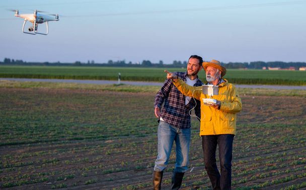 Άνδρες που χρησιμοποιούν σύγχρονη τεχνολογία για την έρευνα της γης που στέκεται στο πεδίο χρησιμοποιώντας drone - Φωτογραφία, εικόνα