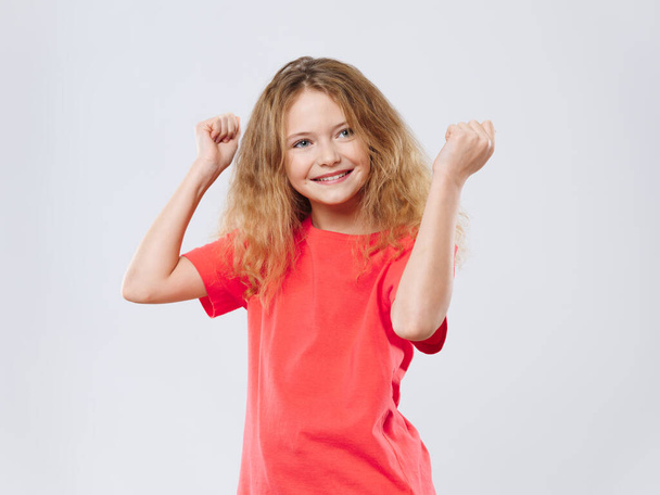 felice ragazza riccia in una t-shirt rossa sta ballando su uno sfondo leggero divertimento gioia emozioni - Foto, immagini