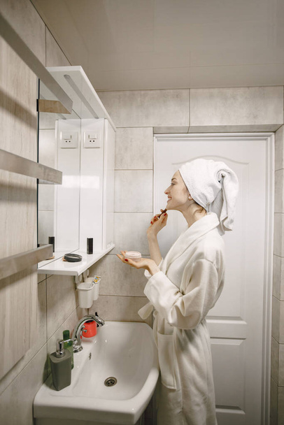 Girl in a white coat and towel takes care of her face in bath - Foto, Bild