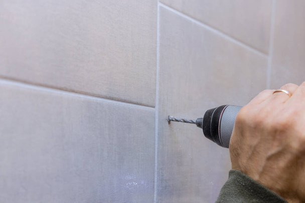 Плотник работает сверление отверстие в стене ванной комнаты для установки аксессуаров для ванной комнаты - Фото, изображение