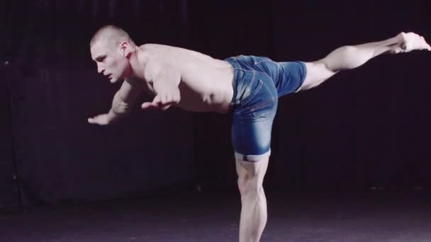 młody pompowany facet w dżinsowych spodenkach wykonuje balansowanie kij Pose - Materiał filmowy, wideo