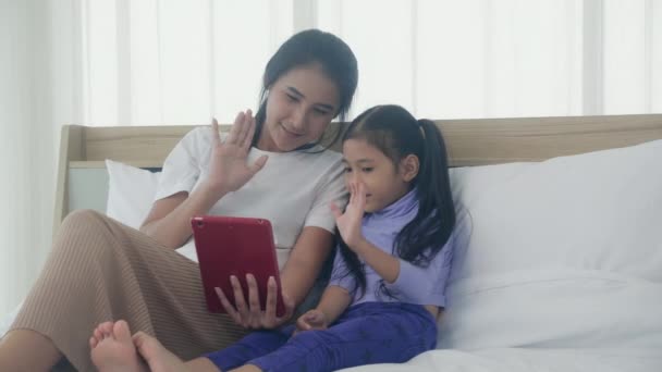 Young asian mom and daughter video call on tablet computer greeting with family together, happy mother and girl with relationship using technology in communication to internet online, two people. - Footage, Video