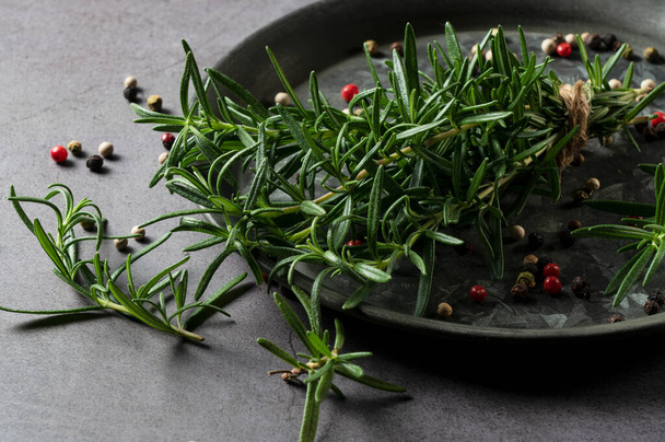 A bunch of fresh rosemary and pepper mix on an iron plate set against a dark background. Image of herbs. - Fotó, kép