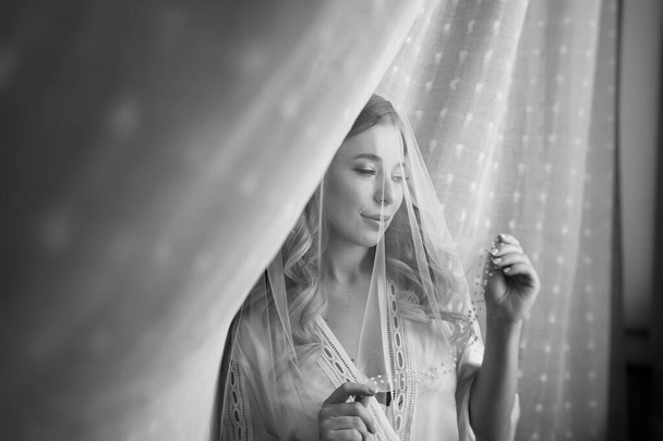 gentle morning of the bride. beautiful young woman in veil under a white curtain - Foto, Bild