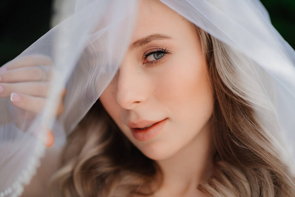 beautiful bride with long wavy hair under the veil. Wedding make-up.  - Foto, afbeelding