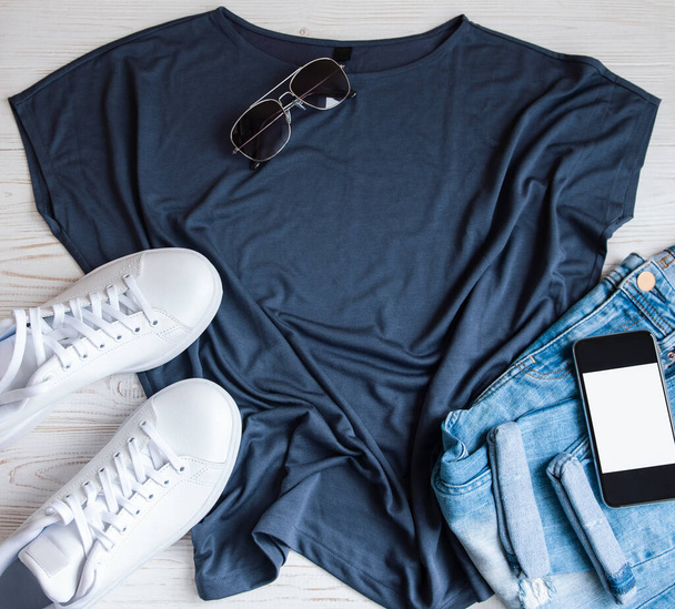Elegante conjunto de ropa femenina. Traje de mujer sobre fondo de madera. Camiseta azul, zapatillas blancas y gafas de sol. Piso tendido, vista superior - Foto, imagen