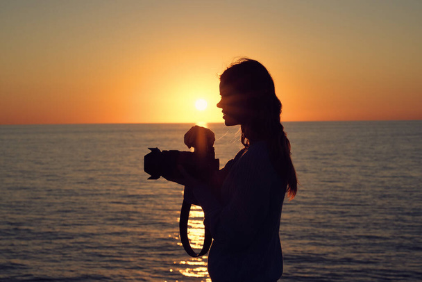 жінка-фотограф з камерою на заході сонця і моря на задньому плані
 - Фото, зображення