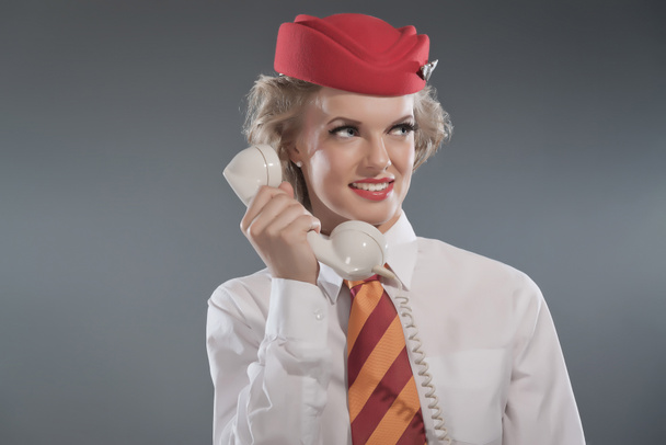 Sonriente retro rubia azafata con gorra roja con corbata a rayas
 - Foto, Imagen