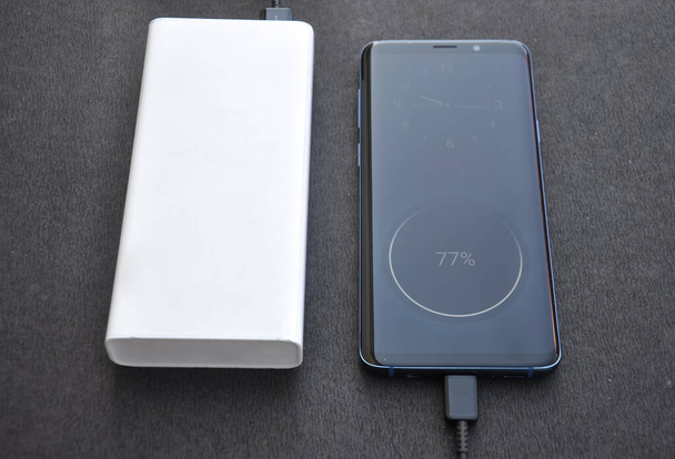 Фото смартфона черного цвета, подключенного к энергобанку для зарядки с черным фоном  - Фото, изображение