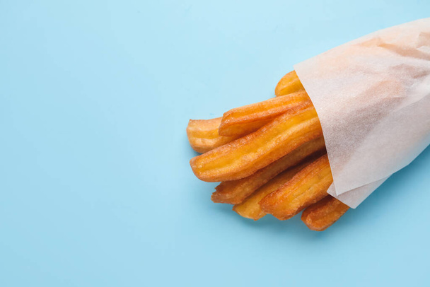 Tasty churros in parchment on color background - Foto, afbeelding