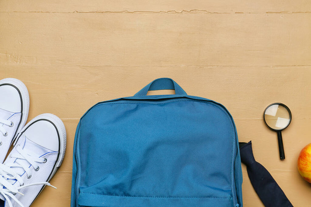 School backpack, shoes and magnifying glass on color wooden background - 写真・画像